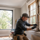 Artisan rénovant une ancienne fenêtre en bois dans une maison lumineuse pour illustrer la rénovation plutôt que le remplacement des fenêtres